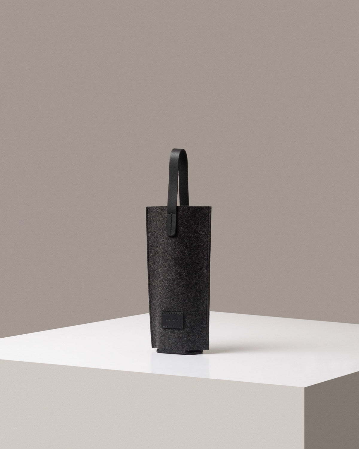 A stylish Hana Merino Wool Bottle Bag in dark gray, displayed in a three-quarter view on a white base