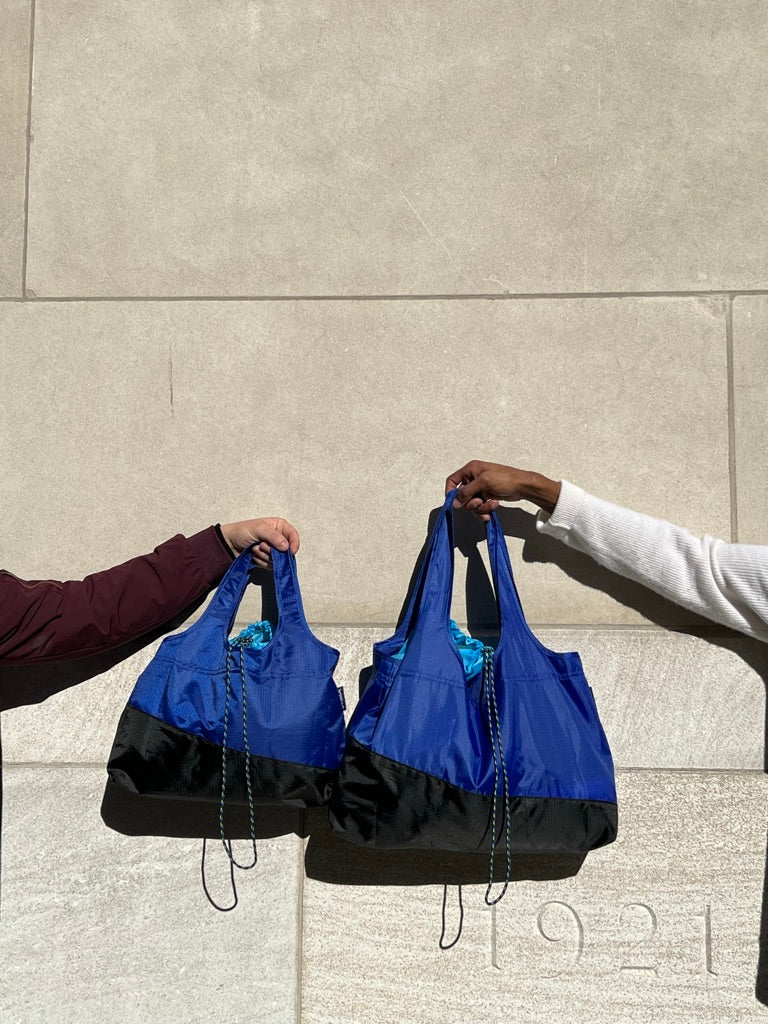 hands from two different people holding two sizes of deep blue bags