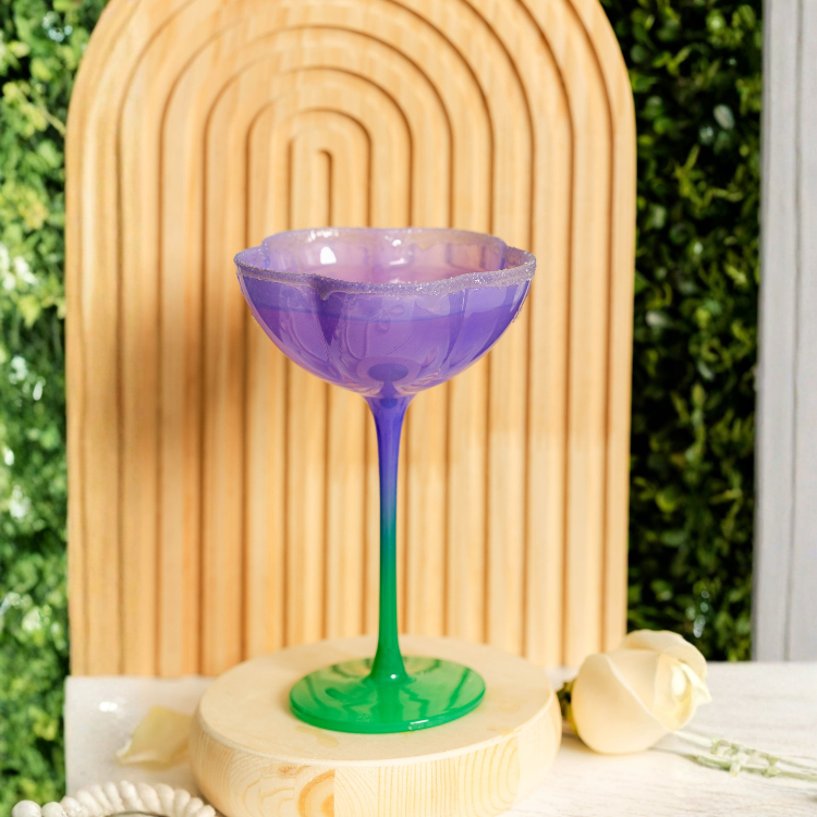 Colorful cocktail glass with a gradient from purple to green on a decorative stand.