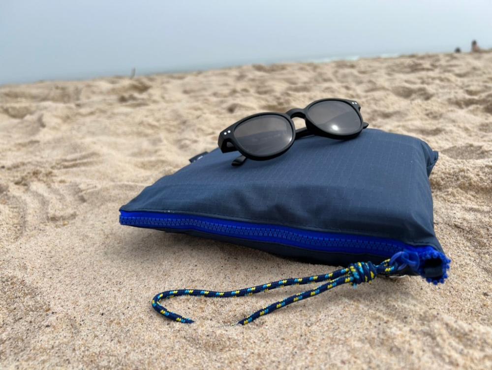 navy pouch in the sand at the beach with sunglasses