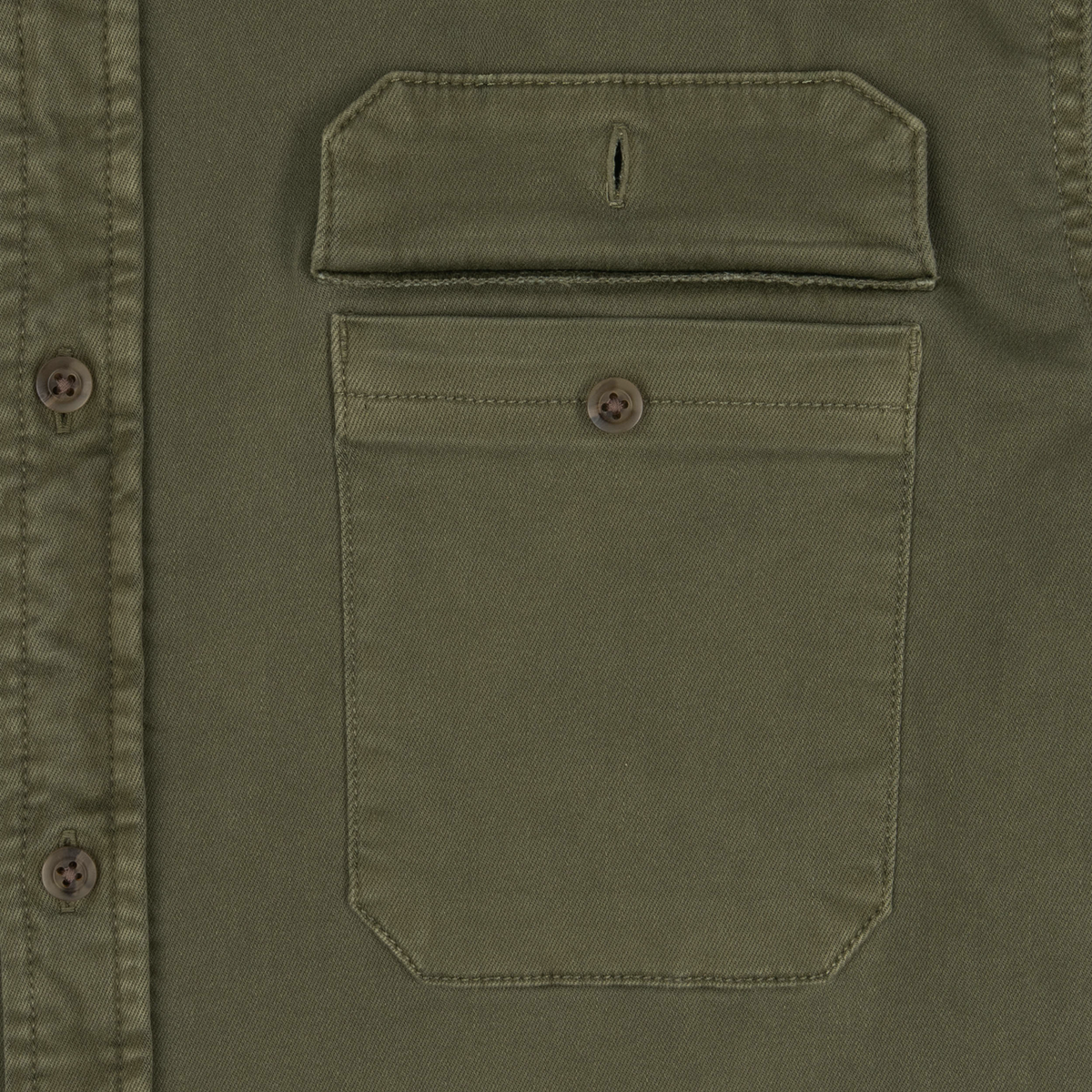 Close-up of an olive green shirt pocket with a flap and button detail from The Buck Snort collection.