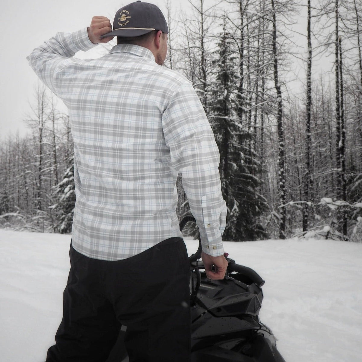 Man wearing grey and blue flannel on snowmobile