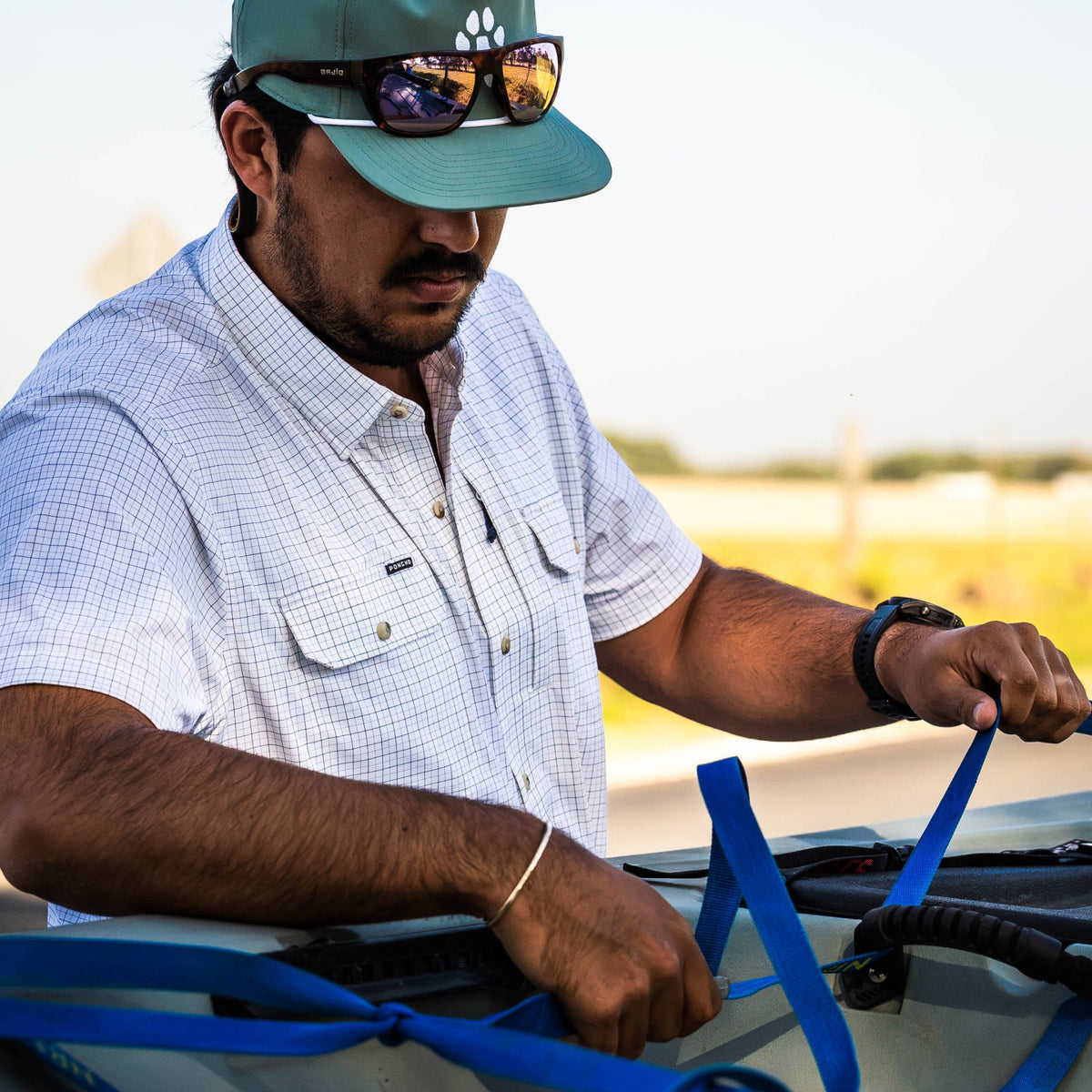 Man in a checked shirt and cap securing blue straps on an outdoor boat
