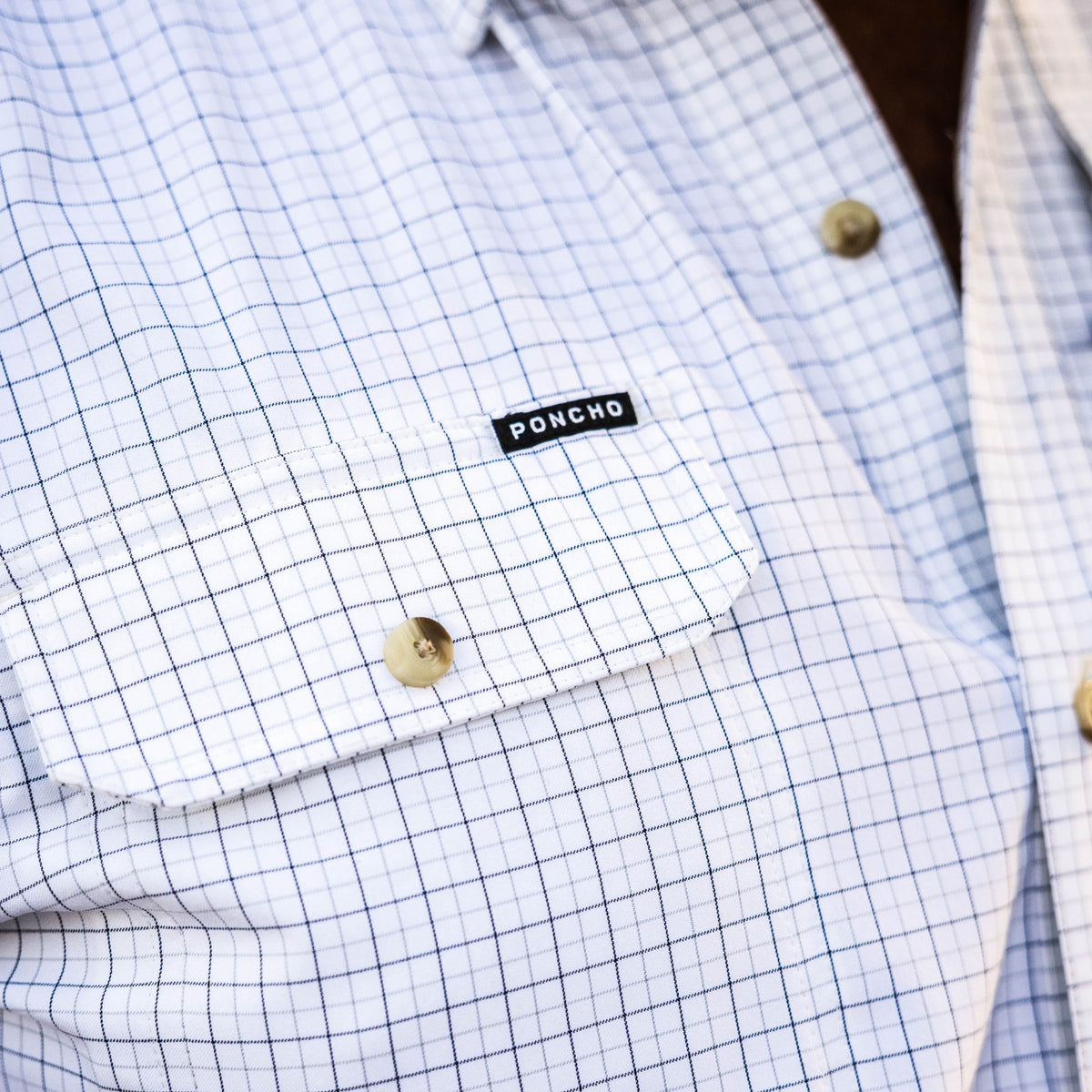 Close-up of a white grid-patterned shirt with wooden buttons and a Poncho label