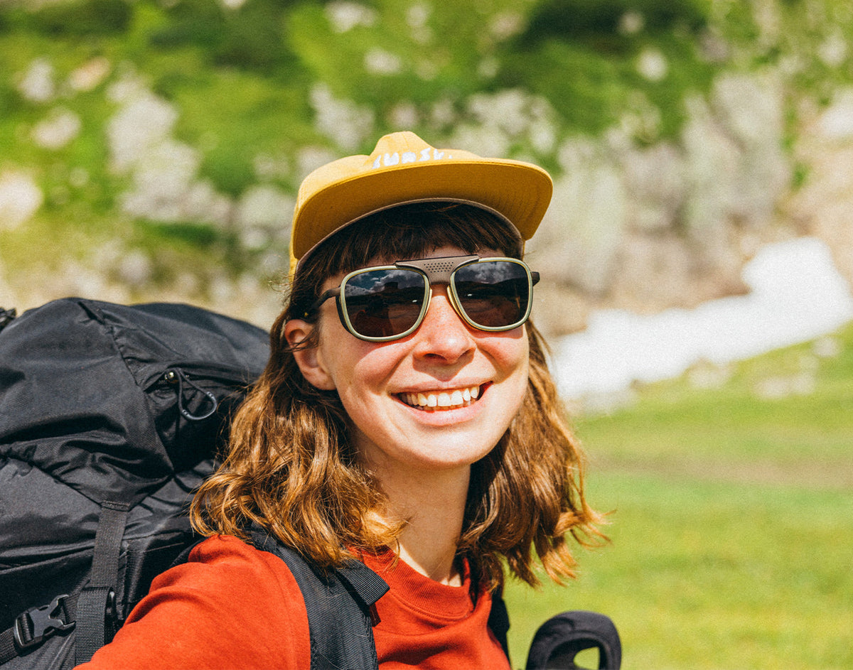 STORY woman backpacking in the mountains wearing sunski ferrata olive citrine amber