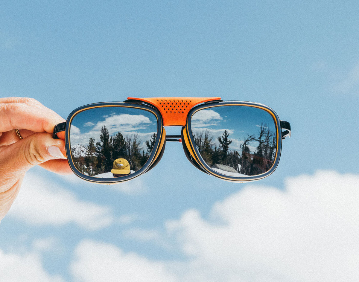 STORY Sunglasses with reflective sky and tree pattern held against a blue sky background