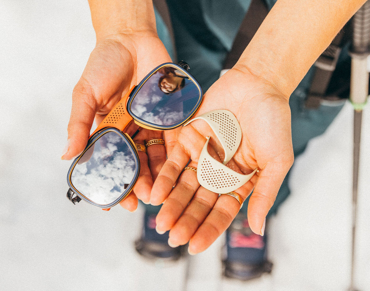 STORY Person holding two pairs of sunglasses with reflective lenses.