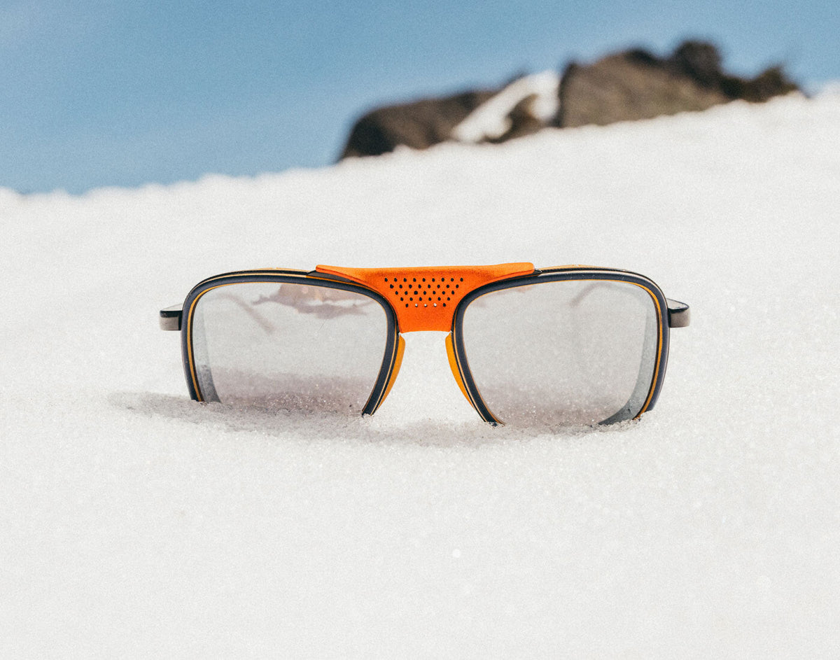 STORY Sunglasses with orange frame and black lenses on a snowy surface
