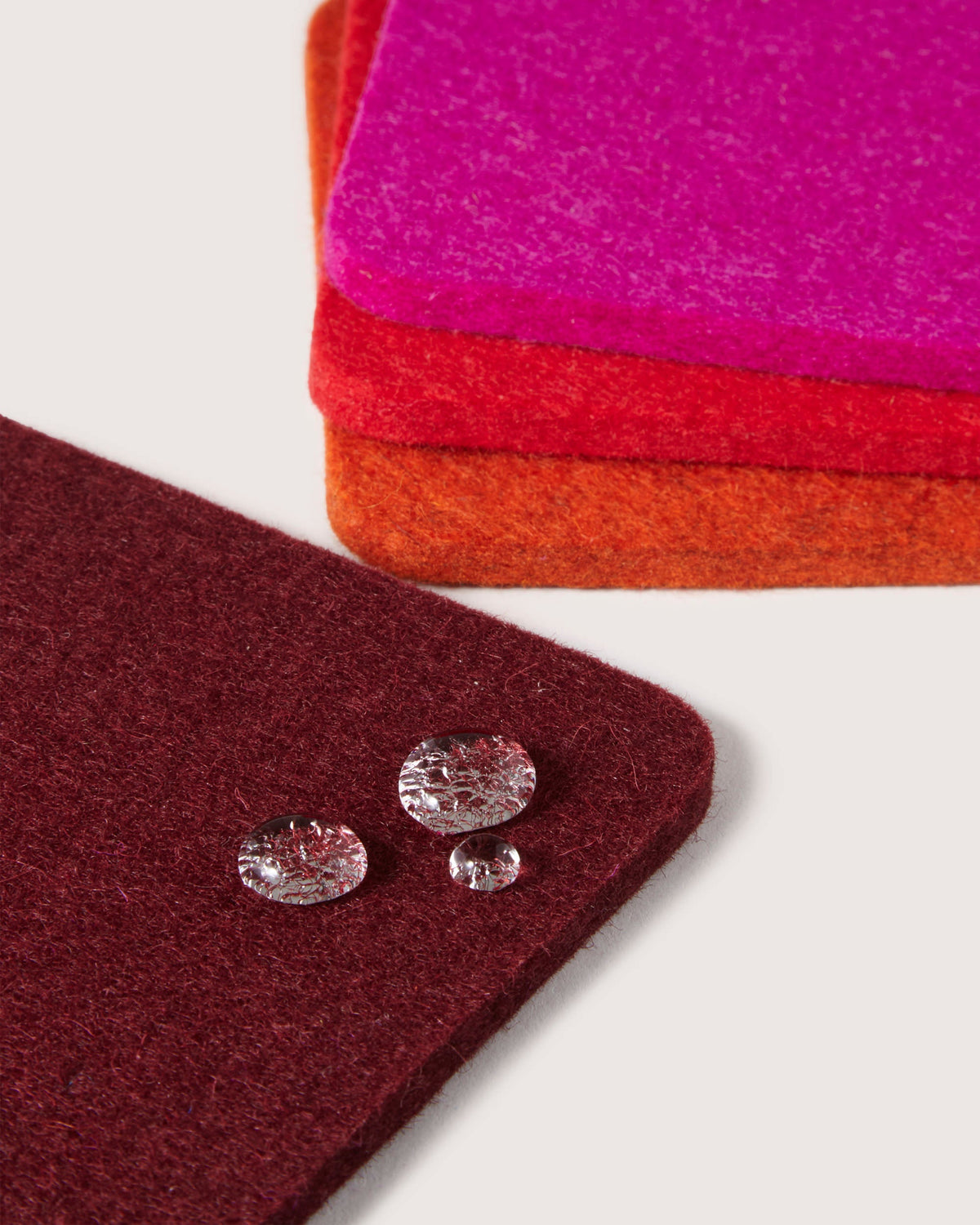 A stack of fabric swatches in red, orange, and pink with crystal-like buttons on the red one showcases minimalist design and rich Merino wool textures against a neutral background, representing graf lantzs aesthetic.