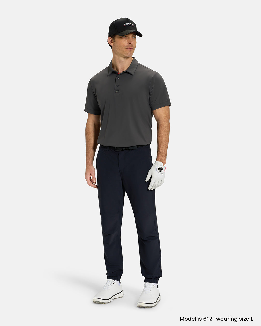 Full Body View of Iron Grey Ghost Golf Core Polo Tucked on White Male Model wearing black pants white gloves black belt white shoes and black hat #color_iron-grey