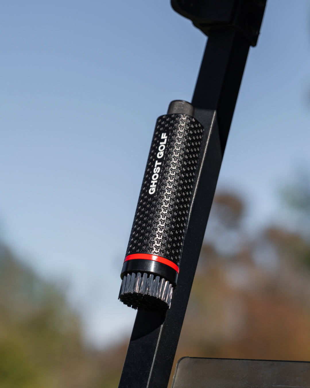 Close-up the Ghost Golf golf brush with 'Ghost Golf' branding against a blurred natural background attached to the golf cart post magnetically #color_navy