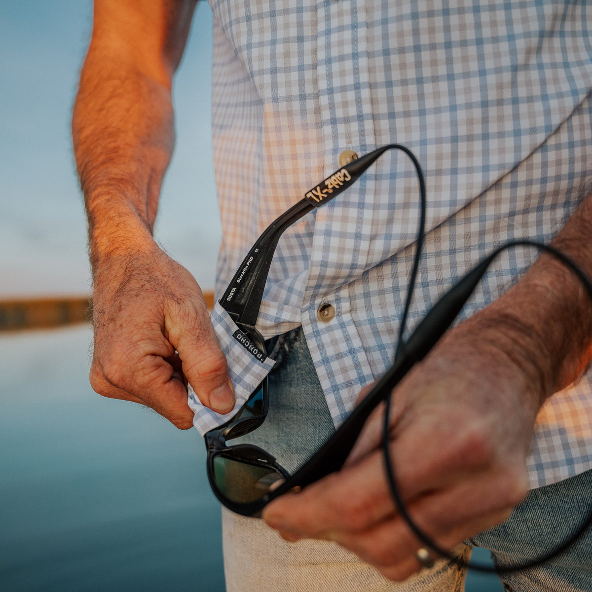 cleaning sunglasses in grey and blue plaid shirt