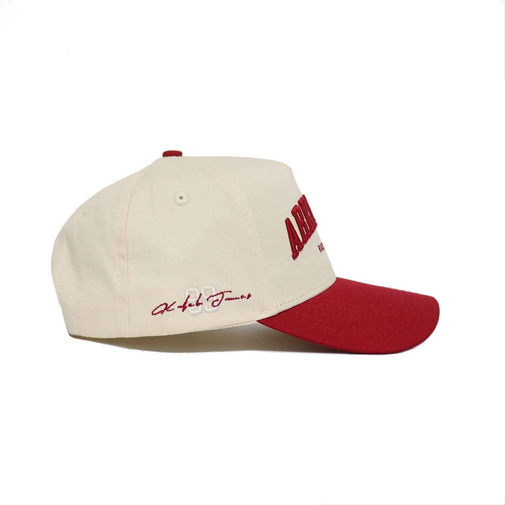 The No Rivals Arkansas Razorback Hat is a cream-colored cap with a red brim and red embroidered text on the front and side, featuring a Snap Back Adjustment for the perfect fit, shown from the side against a white background.