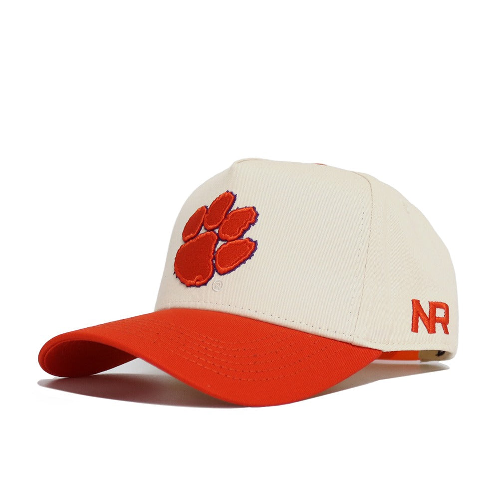 The Classic Clemson Hat by No Rivals is a white cotton baseball cap with an orange brim, orange paw print logo on the front, and NR embroidered in orange on the side, offering a comfortable fit for gameday.