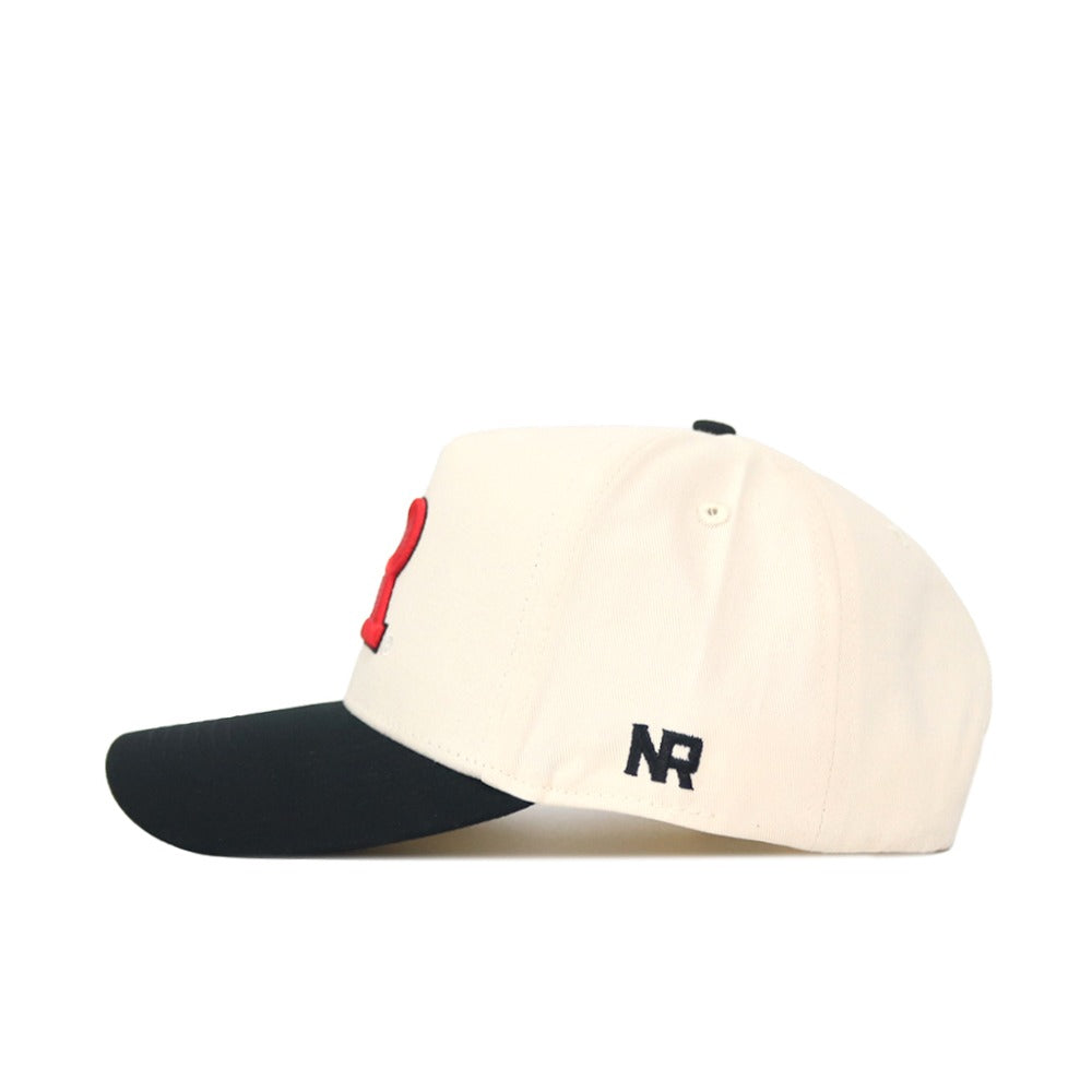 The Classic Rutgers Hat (B2B) by No Rivals is a cream snapback baseball cap featuring a black curved brim, red front lettering, and stitched black NR initials above the ear. Made from high-quality cotton, shown in left side profile.