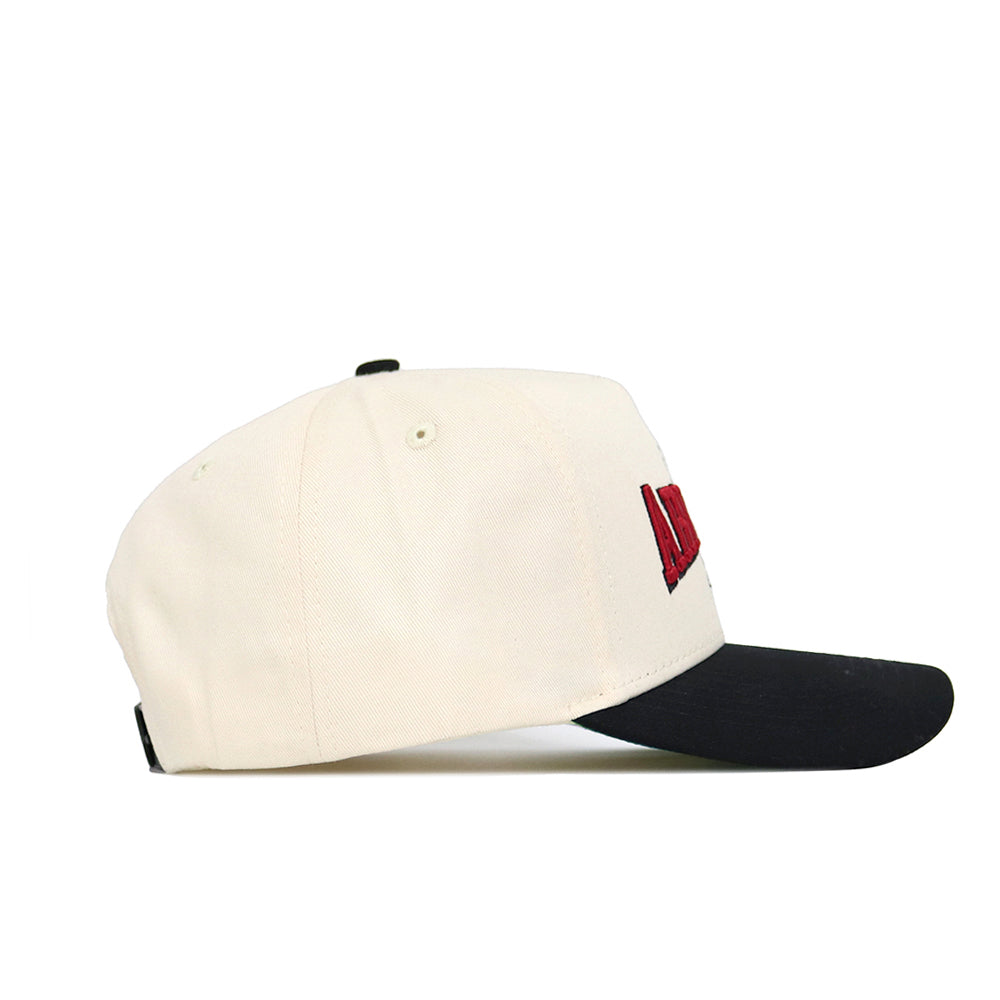 The Arkansas Ballpark Hat by No Rivals is a white cotton baseball cap with a black bill, side view shown. It features red embroidered letters on the front and two ventilation eyelets on the side.