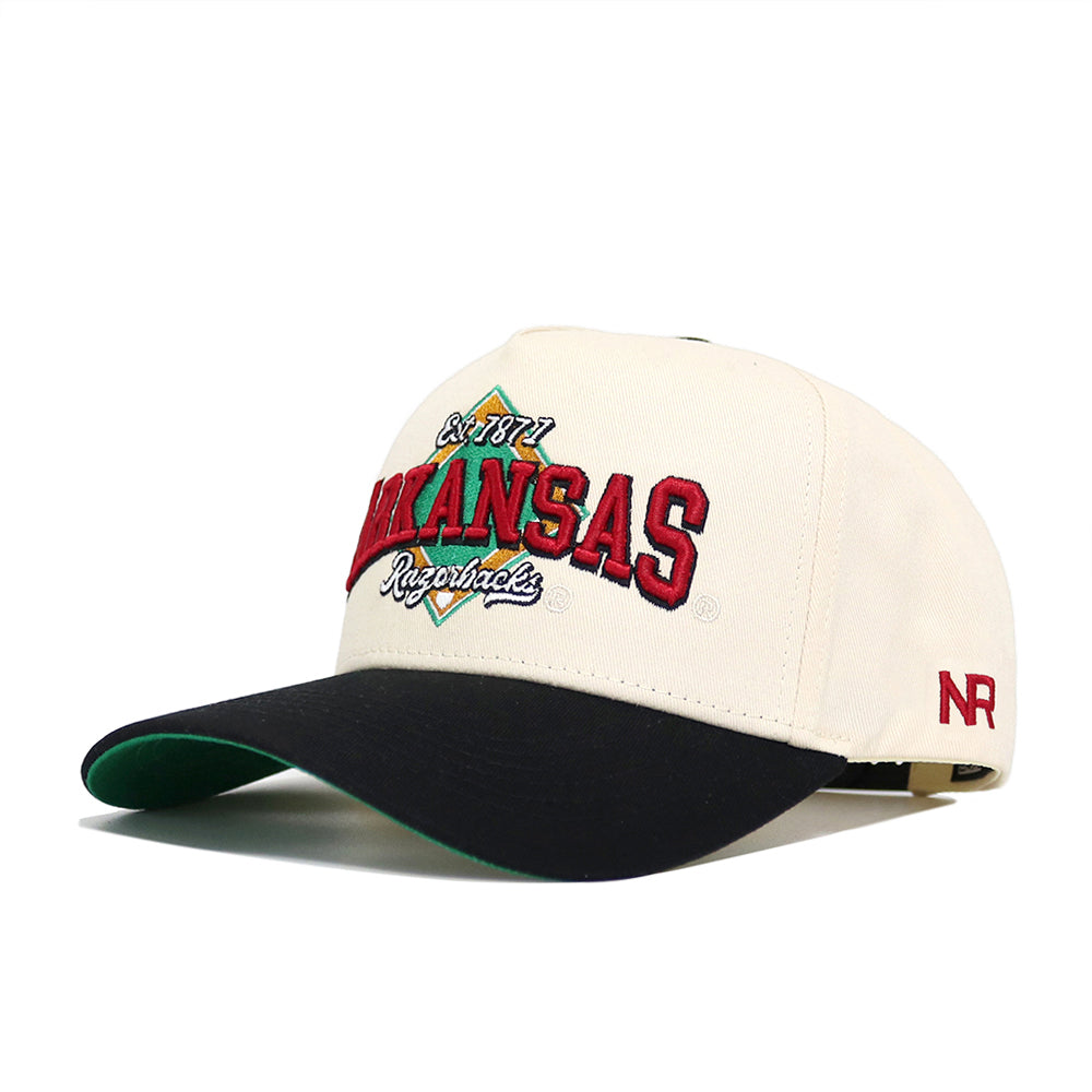 The Arkansas Ballpark Hat by No Rivals is a white and black snapback featuring “Arkansas Razorbacks” in red and black, a green underbill, and “NR” stitched in red on the side. Made from high-quality cotton for lasting comfort.