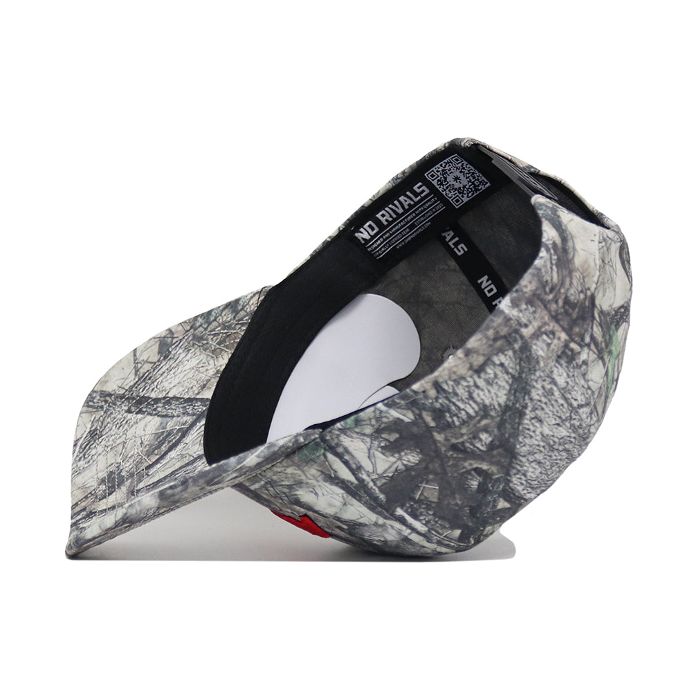 The Arizona Outland Hat by No Rivals, a camo-patterned snapback, is pictured upside down on a white background, displaying its inner lining, QR code tag, and "NO RIVALS" text along the interior band.