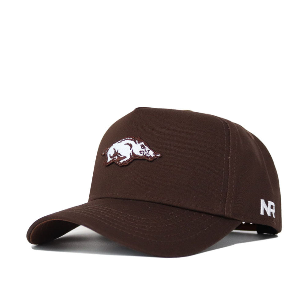 The Arkansas Americano Hat is a brown cotton snapback cap with an embroidered white razorback logo on the front and NR initials on the side. This licensed hat offers a comfortable, structured fit for everyday wear.