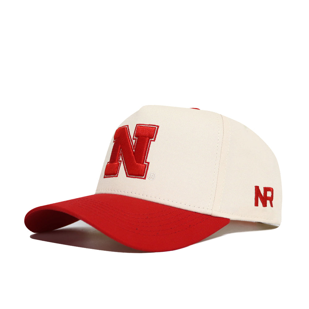The Classic University of Nebraska Hat by No Rivals is a white cotton cap with a red bill, a bold red "N" on the front, and "NR" embroidered in red on the side, offering comfort and durability.