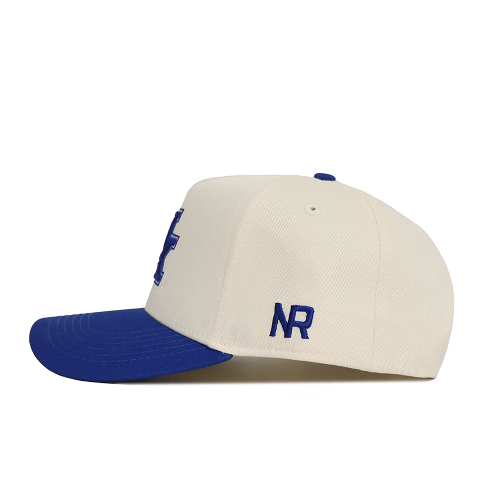 The Classic University of Kentucky Hat by No Rivals is a cream snapback with a structured fit, blue brim, blue NR initials above the ear, and a blue front design partly visible from the side.