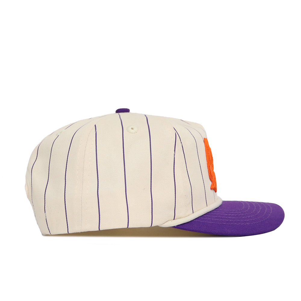 The Clemson Pinstripe Hat by No Rivals features cream cotton with thin purple stripes, an orange letter on the front, a solid purple brim, and a snapback design. Shown in a stylish side profile view.