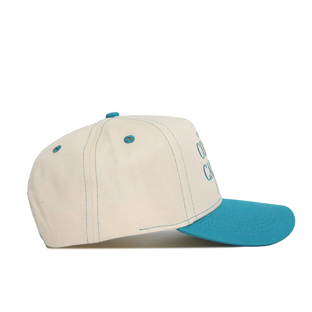 The No Rivals Coastal Carolina Vintage Hat is a beige snapback with teal blue eyelets, button, and brim, shown side view on white. Made from high quality cotton in a structured fit, it displays partially visible blue text on the front.