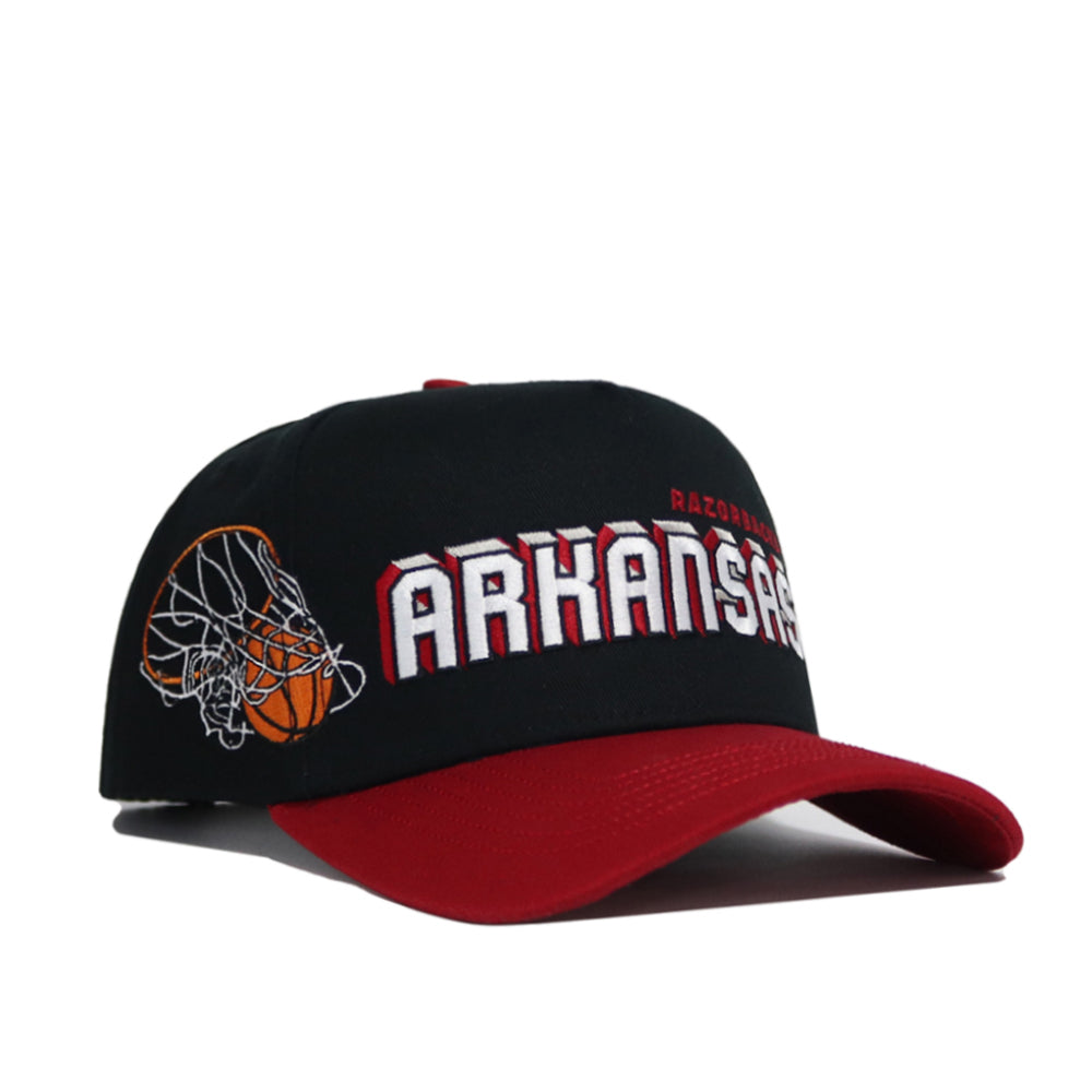 The Arkansas Courtside Hat is a black and red snapback with "Arkansas" and "Razorbacks" embroidered on the front, plus a basketball and net graphic on the side. Made from high-quality cotton for a structured fit.