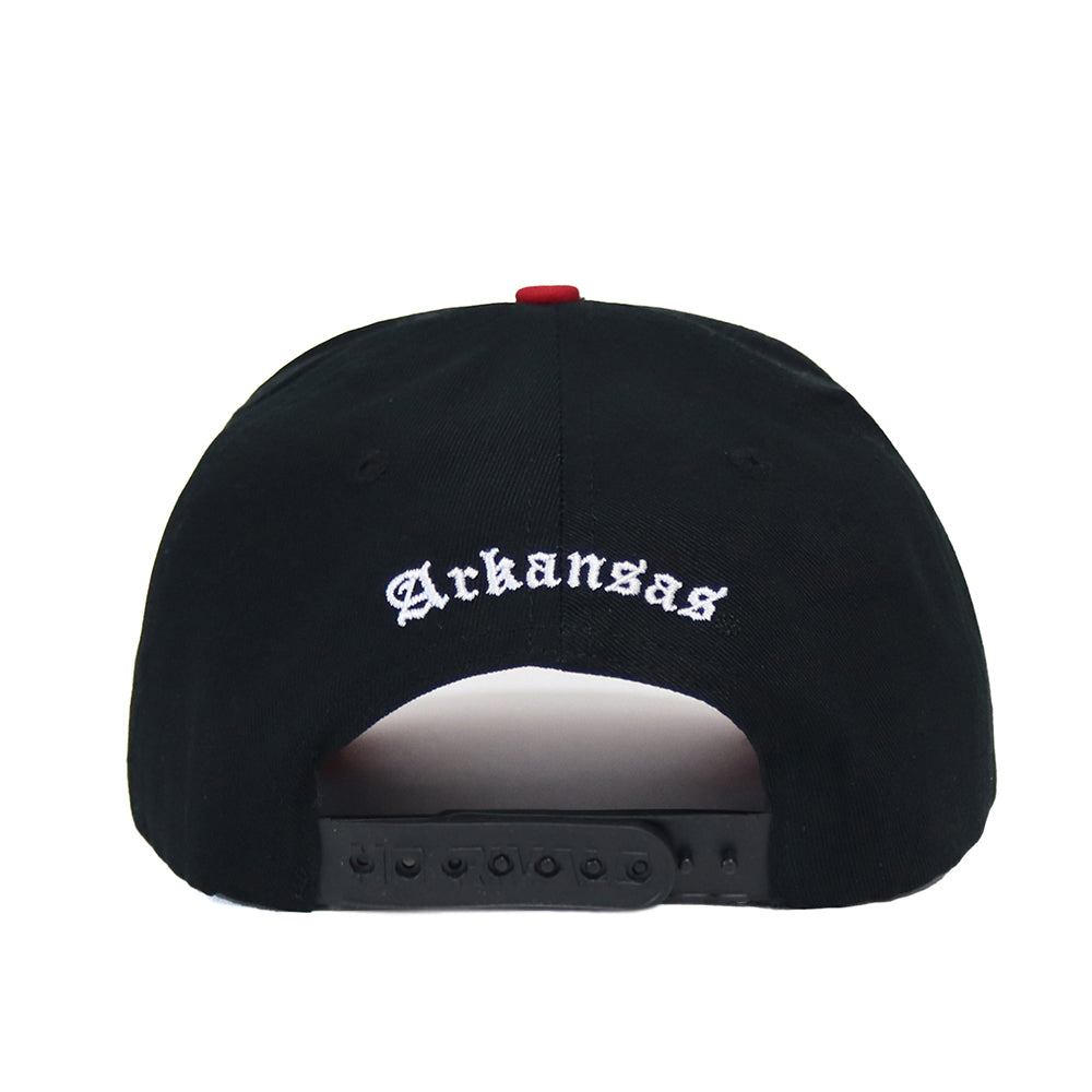 The Arkansas Courtside Hat is a black snapback featuring "Arkansas" embroidered in white gothic letters above the adjustable strap, seen from the back and offering a structured fit.