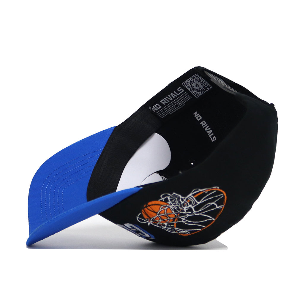 The BYU Courtside Hat is a black and blue snapback, shown tilted on its side. Made from high quality cotton, it features a basketball and net graphic on the front and "NO RIVALS" printed on the inner band.