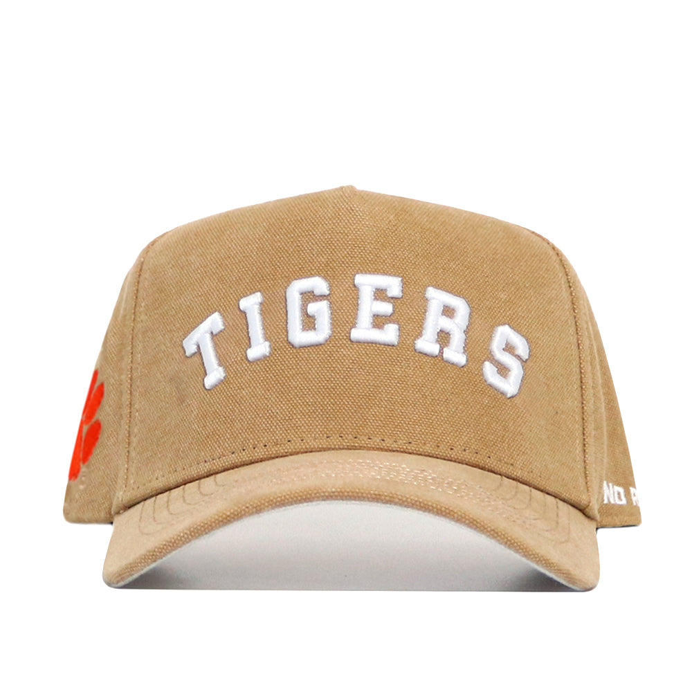 The Clemson Rustic Hat by No Rivals is a tan snapback cap with "TIGERS" in white on the front, an orange paw print on the left side, durable cotton canvas construction, and is officially licensed.