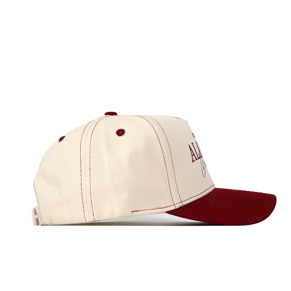 The Alabama Vintage Hat by No Rivals is a cream-colored snapback with a maroon brim, button, and stitching. Made from high-quality cotton, it features partially visible embroidered text on the front. Side view shown.