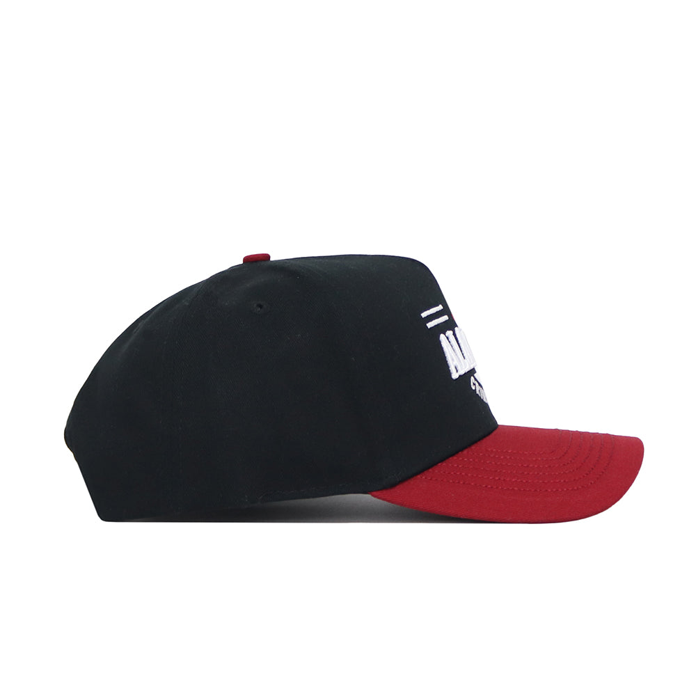 The Alabama Tailgate Hat by No Rivals is a black snapback with a curved dark red brim, seen from the side. Made from high-quality cotton, it showcases white embroidered text and design on the structured front.