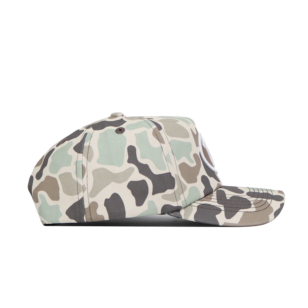 A side view of the BYU Huntsman Hat by No Rivals, a duck camo 5-panel cap in green, beige, brown, and black with a curved brim, snapback closure, and visible stitching on the brim and top.
