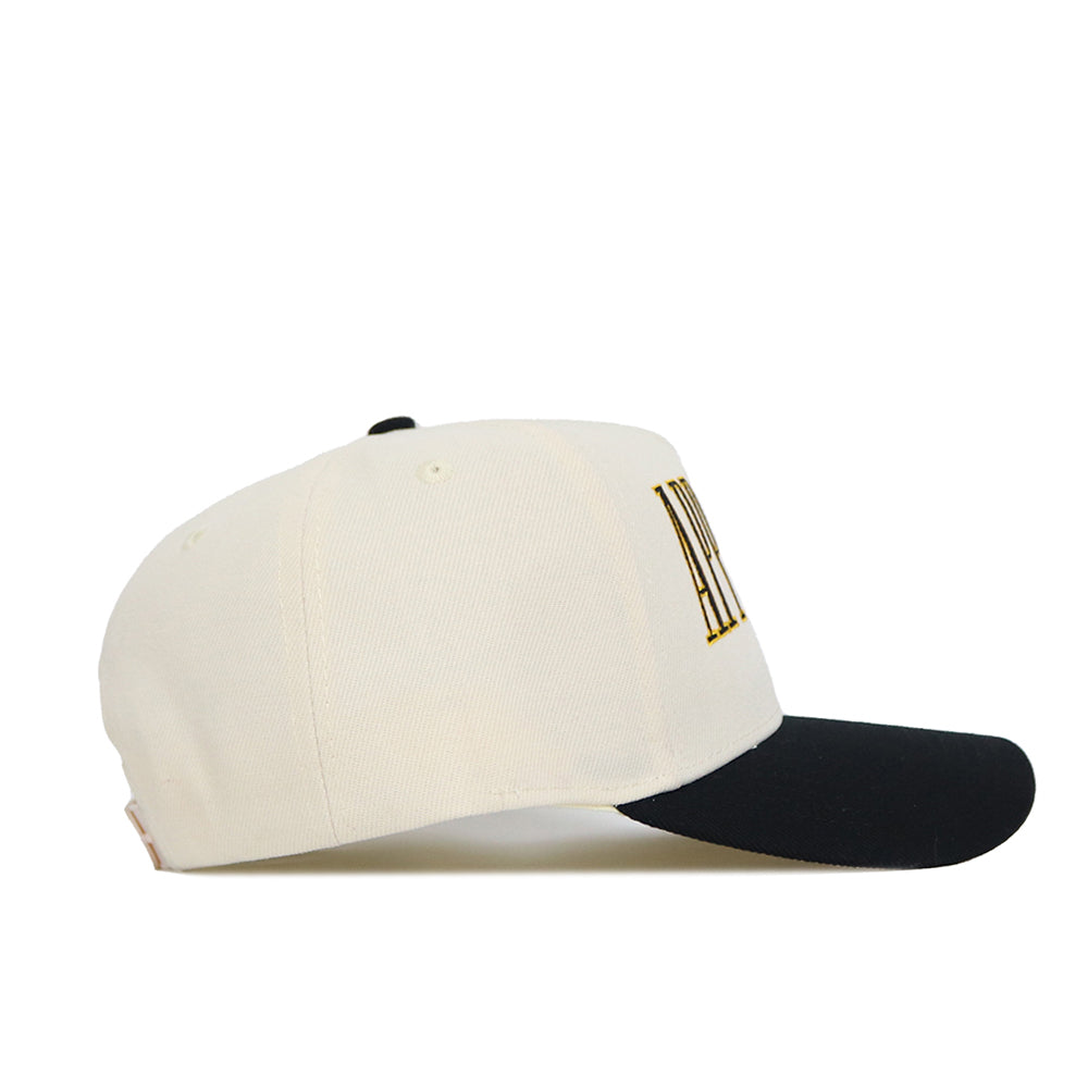 The No Rivals App State Retro Block Hat is a cream snapback with a black curved brim, acrylic wool blend, side ventilation eyelets, and yellow/black embroidered lettering on the front, shown from the side.