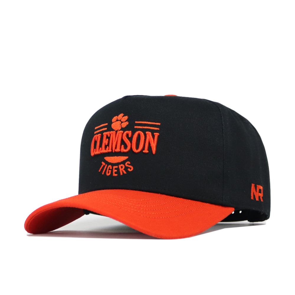 The Clemson Tailgate Hat by No Rivals is a black snapback cap with an orange brim, featuring an orange embroidered Clemson Tigers paw logo on the front and NR stitched on the side. Made from high-quality cotton with a structured fit.