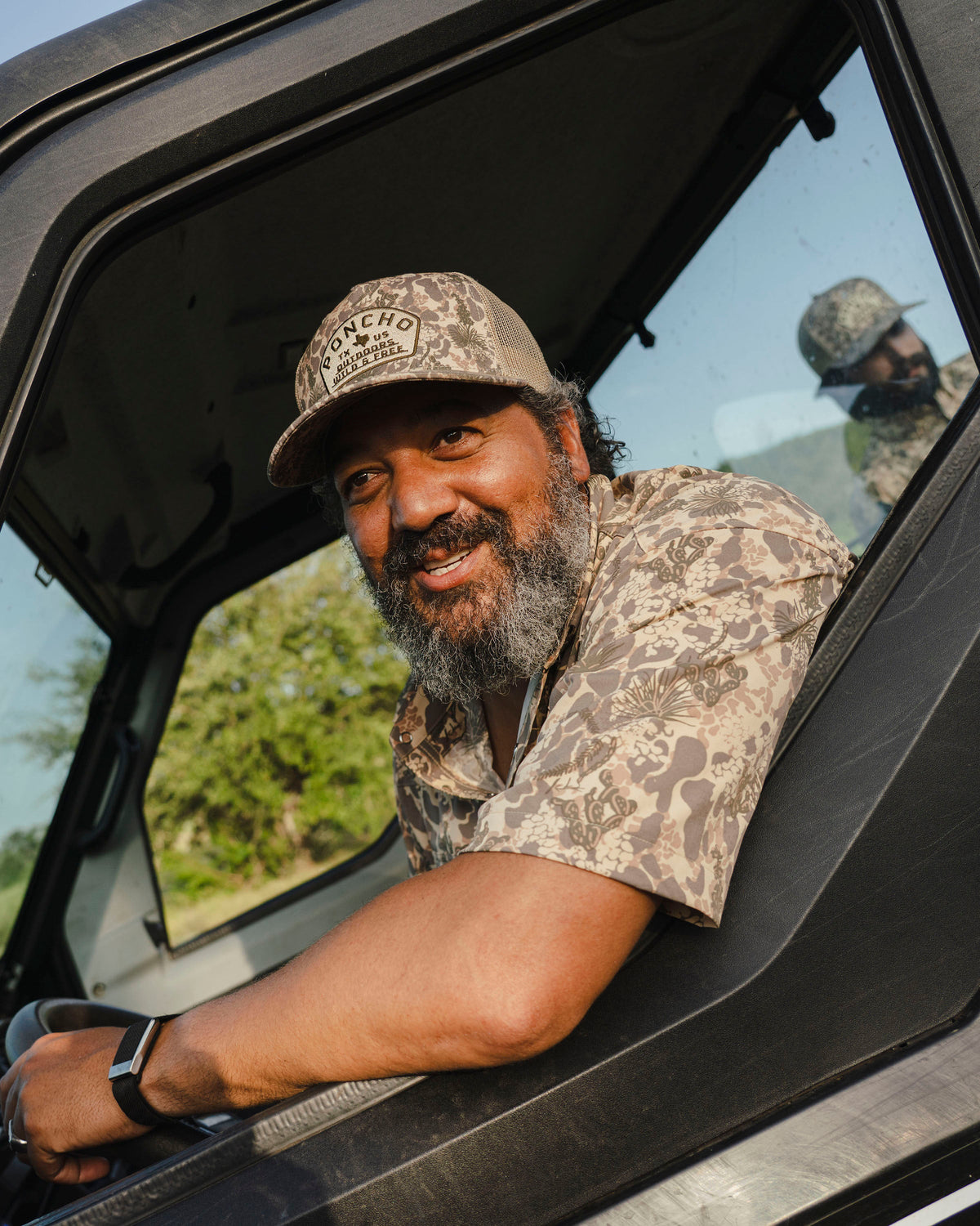 Man wearing "The Albany" shirt with nature-inspired pattern and matching cap, smiling inside a vehicle window.