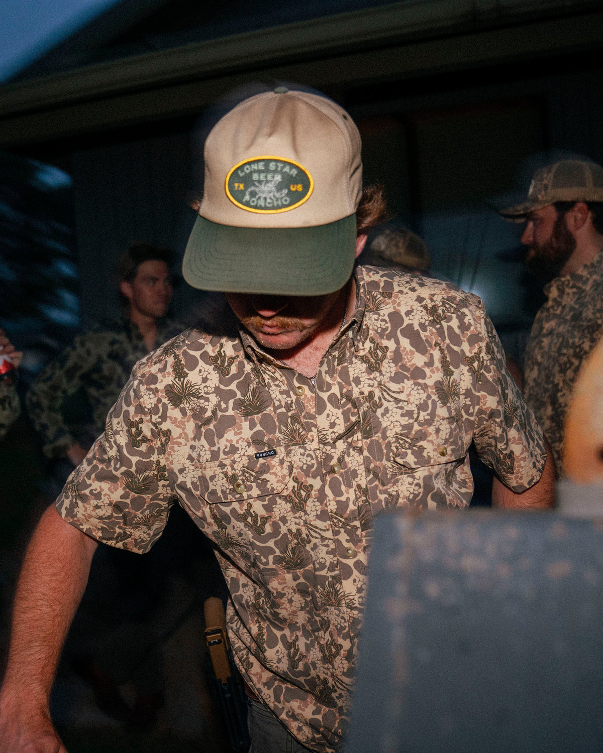 Man wearing The Albany shirt with a nature-inspired camo pattern at an outdoor evening gathering