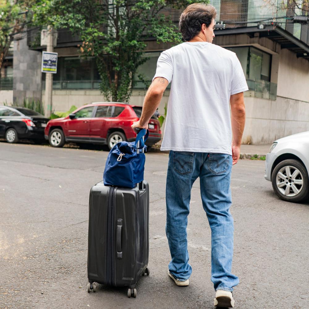 Guy walking with suitcase, balancing navy tote on top of suitcase