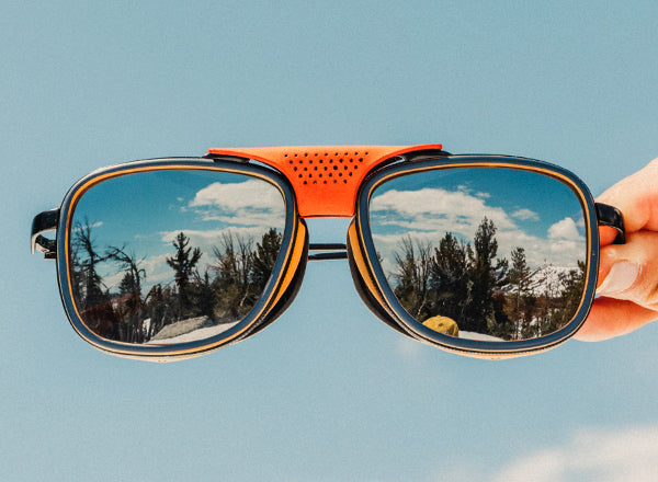 RICH hand holding sunski ferrata sunglasses with reflection of trees in the lenses