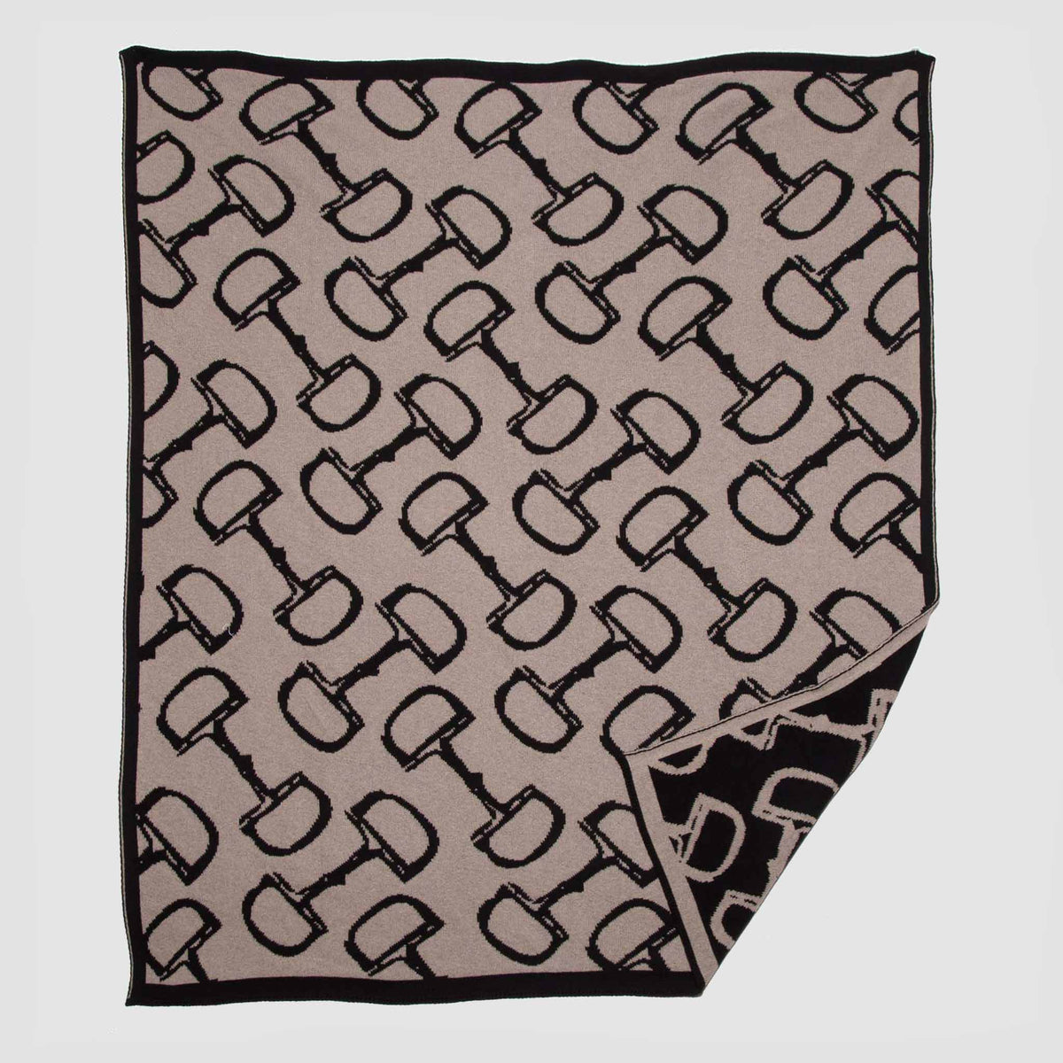 The in2green Reversible Bits - Sustainable Knit Equestrian Throw Blanket is a beige and black reversible throw showcasing a repeating equestrian-inspired pattern, reminiscent of a cozy country house, with one corner flipped to display the reverse side of the design.