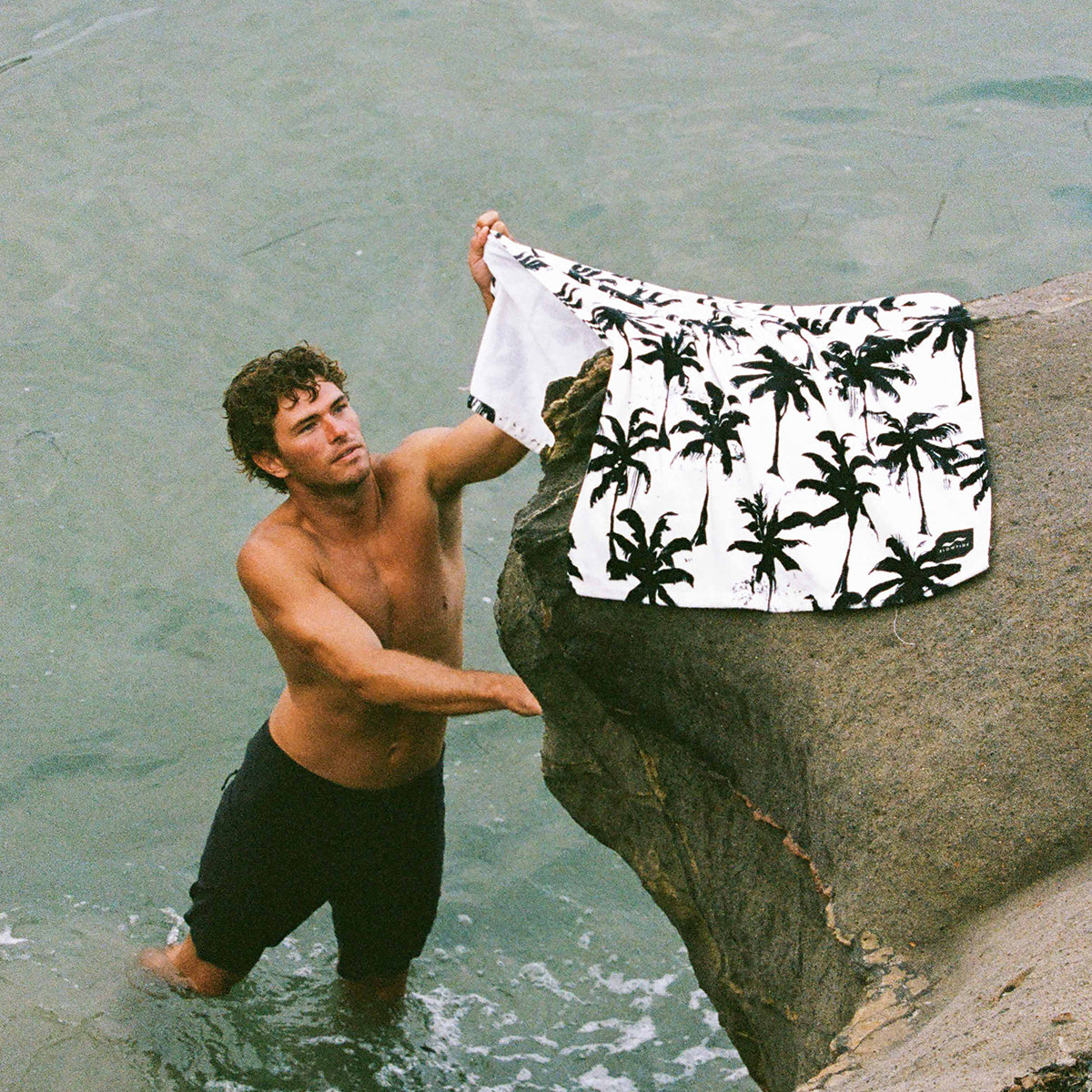 Velour towel with printed pattern absorbing moisture, draped on a rock by the shore.