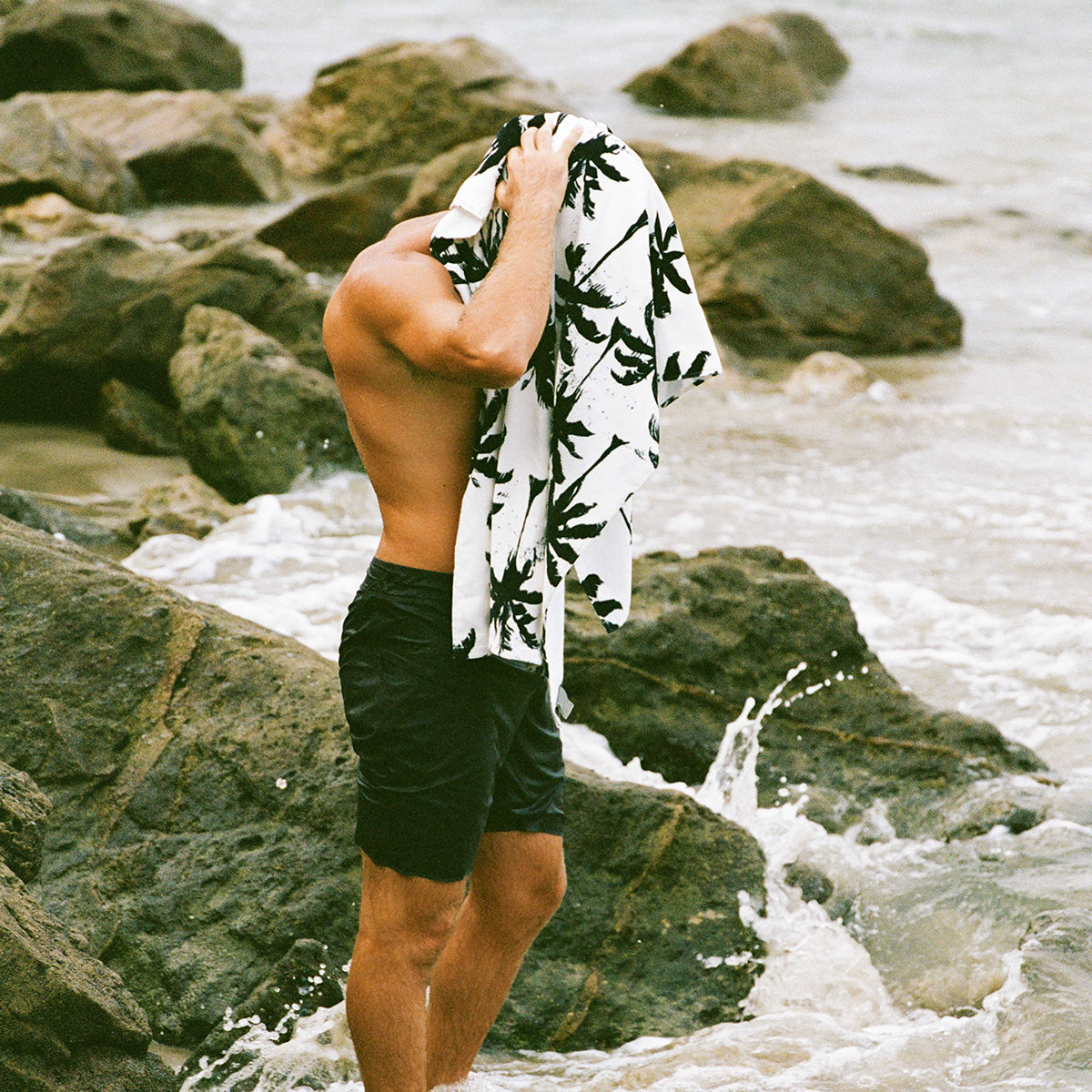 Velour towel with black leaf print pattern shown on coastal rocks.
