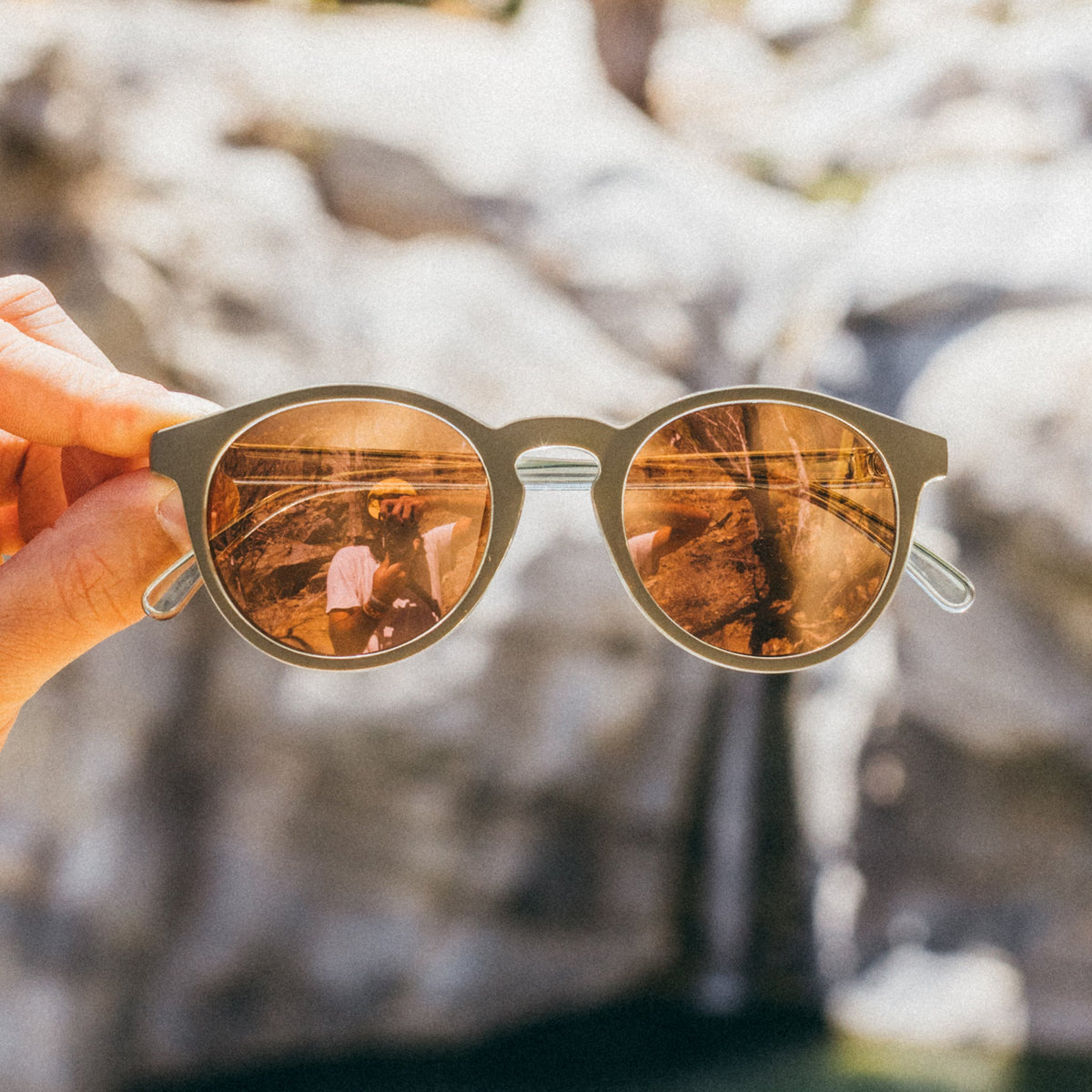 Sunglasses with reflective lenses held against a natural background