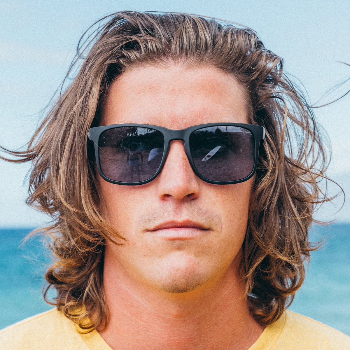 Man with sunglasses and long hair against a blue sky background