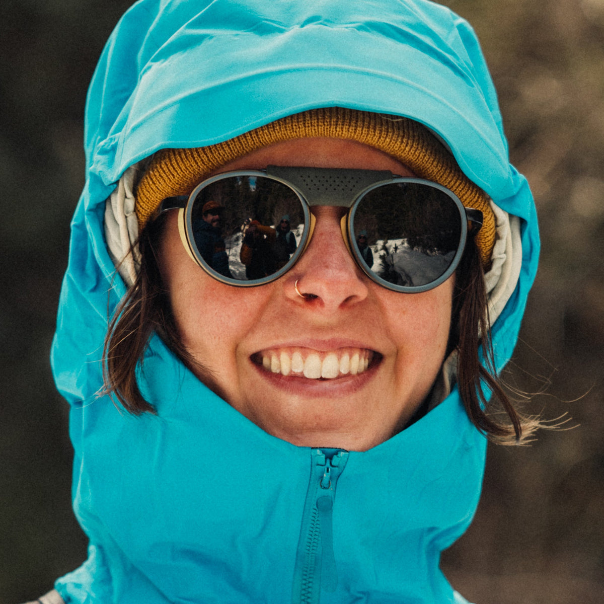 Person wearing a blue hooded jacket and sunglasses with a blurred background