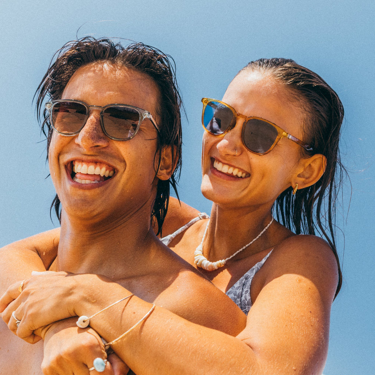 Two people with sunglasses smiling against a clear blue sky