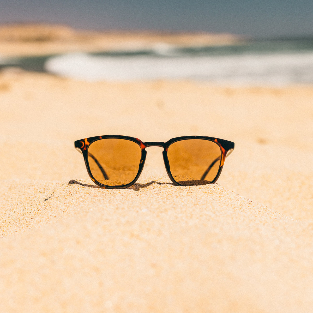 Sunglasses on a sandy beach with ocean in the background