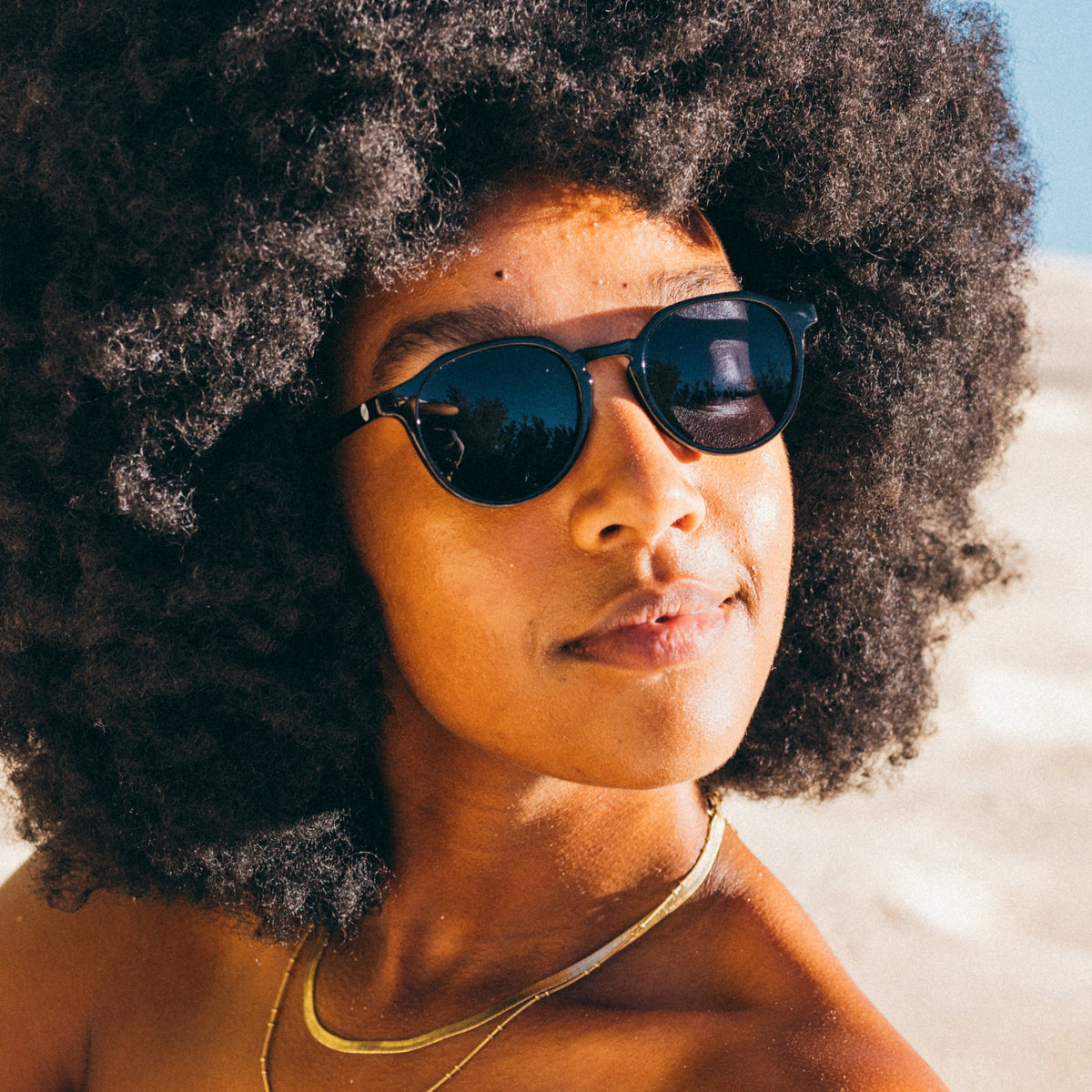 Person with an afro wearing sunglasses on a beach