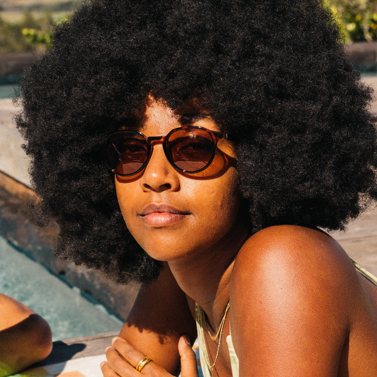 Woman with an afro wearing sunglasses by a pool